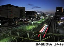 線路に電車の赤いライトが光っている様子を高所から撮影した写真に、夜の春日部駅付近の様子と説明書きされている写真