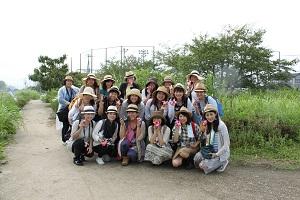 麦わら帽子をかぶったツアー参加者たちが屋外で3列に並び記念撮影している写真