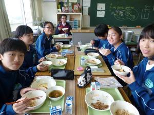 青いジャージを着た生徒たちが机をくっつけて給食を食べている写真