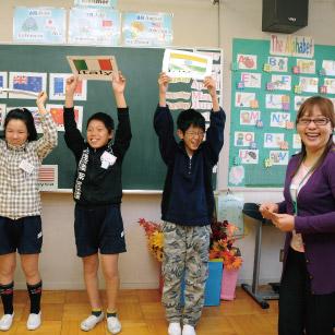 国旗と国名が英語で書かれた札を挙げて発表する児童の写真