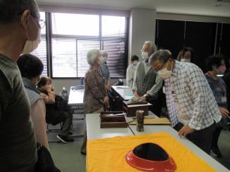 机の上に黄色いクロスが敷かれ、その上に置かれた増村さんの作品を受講者が眺めている写真