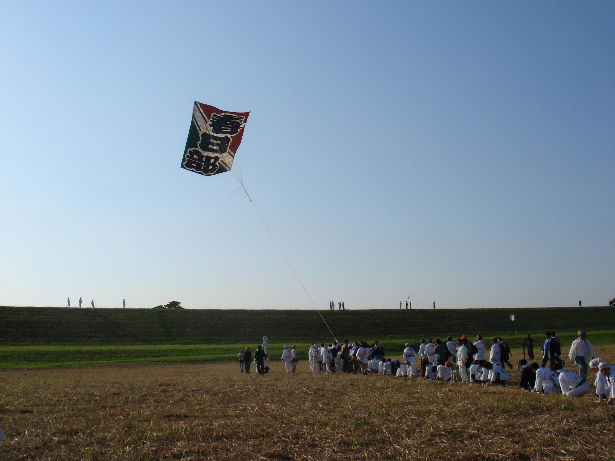 多くの人が協力して、春日部と書かれた大きな凧をあげている写真