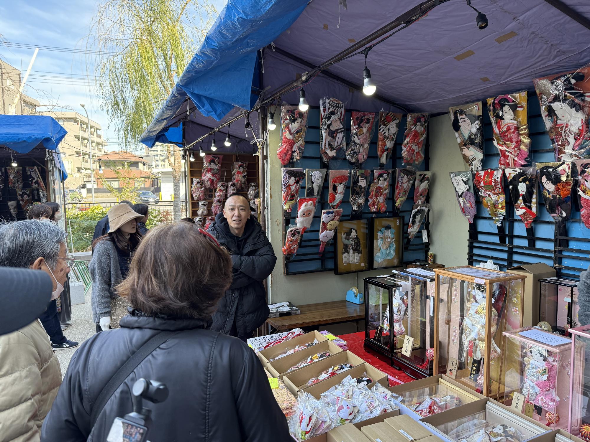 カラフルな羽子板がたくさん並んでいる店で、店員と商品を選んでいる客がいる写真