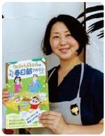 エプロンをつけた志村美智子さんが、チラシを持って微笑んでいる写真