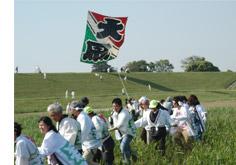 緑の平野でたくさんの参加者たちが大凧あげをしている写真
