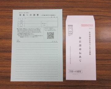 机の上に、記入欄のある提言用紙と、春日部市長あてと書かれたピンク色の封筒が並んでいる写真