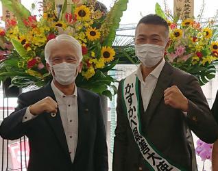 オープン祝いの花を背景に内山さんと石川市長がガッツポーズを作り笑顔をみせる写真