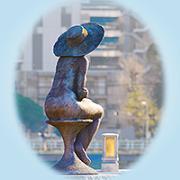 川岸に座り街並みを見つめる女性の銅像の写真