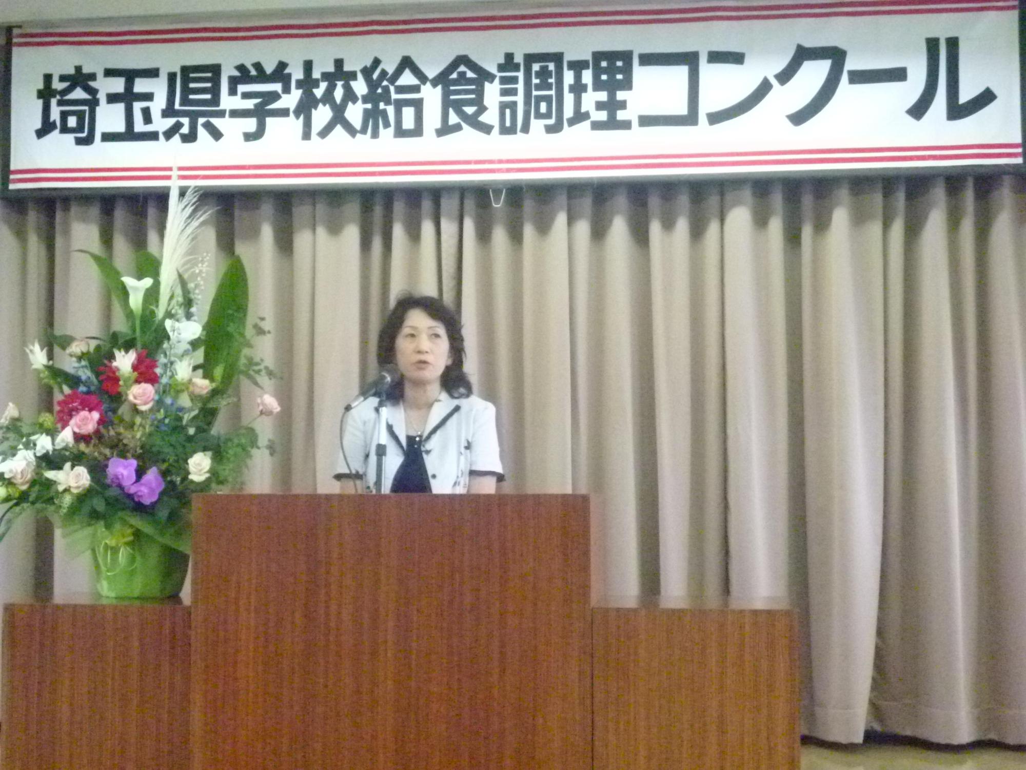 埼玉県学校給食調理コンクールの壇上に立ち話をする女性の写真