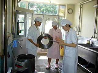 鍋の蓋を手に持ち衛生チェックを行う調理員と栄養士の写真