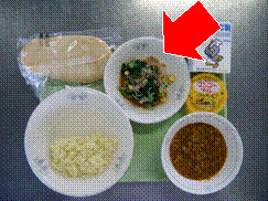 お盆に載せられた給食の青菜とじゃこのサラダのお皿を矢印で示した写真