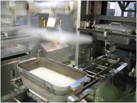 調理場でバットに入ったお米が機械で炊飯される様子の写真
