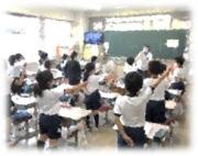 教室で多数の生徒が手を挙げている写真