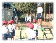 赤い帽子を被った生徒が並んでいる前で青い帽子を被った生徒が壇上に立っている写真