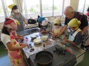 三角巾を被った人たちがキッチンでお菓子を作っている写真