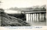 写真奥から流れている川に橋がかかっている風景の白黒写真