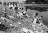 河川敷に集まって清掃を行う人々の白黒写真