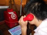 赤色の公衆電話の受話器を耳に当てている生徒の写真