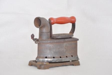 楕円形の鉄製の容器にパイプと取っ手がついている旧型の炭火アイロンの写真