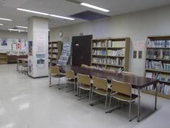 白いフロアと木でできた机と椅子が置かれた武里地区公民館図書コーナーの写真