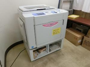 白い印刷機が備え付けられている印刷室の写真