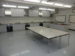 白を基調とした部屋に同じく白を基調としたキッチンと備品が用意されている幸松地区公民館実習室の写真