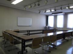窓から光が差し込む武里地区公民館会議室2（机といすを置いた状態）の写真