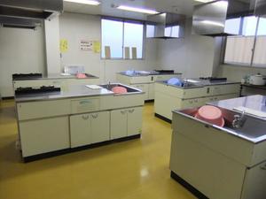 黄色いフロアに調理実習用のキッチンが複数備え付けられている粕壁南公民館調理室の写真