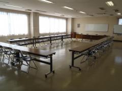 窓から光が差し込む武里地区公民館研修室1（机といすを並べた状態）の写真