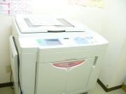 部屋の角に白い印刷機が置かれている庄和南公民館印刷室の写真