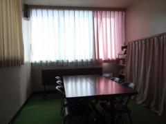 カーテンから差し込む光を部屋中央に置かれた机が反射している武里東公民館:託児室の写真