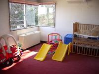 赤紫色のカーペットが敷かれ、カラフルで小さな滑り台が2つ置いてあり、小さな窓から明るい日差しが差し込む様子の内牧南公民館託児室の写真