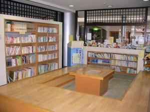 コの字型の木製の椅子が中央に据えられている内牧地区公民館図書コーナーの写真