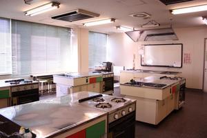 三口コンロが備え付けられてキッチンが複数用意されている実習室の写真